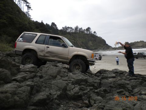 1994 Ford Explorer - A man holds up a fish while standing near a 1994 Ford Explorer on a rocky beach.