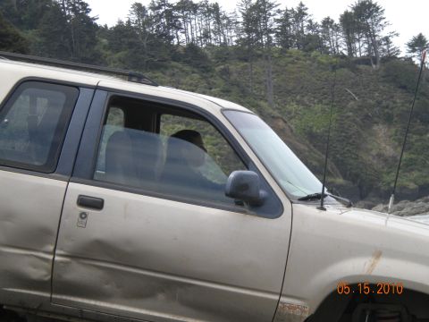 1994 Ford Explorer - SUV with damage on the driver's side, parked near a coastal area with trees.