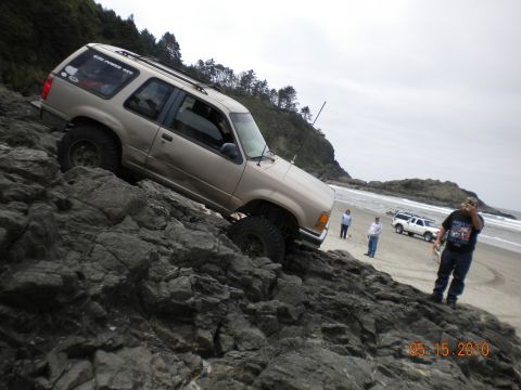 1994 Ford Explorer - A 1994 Ford Explorer navigates a rocky coastal terrain near the ocean, with other vehicles and onlookers present.