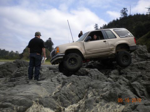 1994 Ford Explorer - A man watches as a modified Ford Explorer navigates a rocky terrain near the coast.