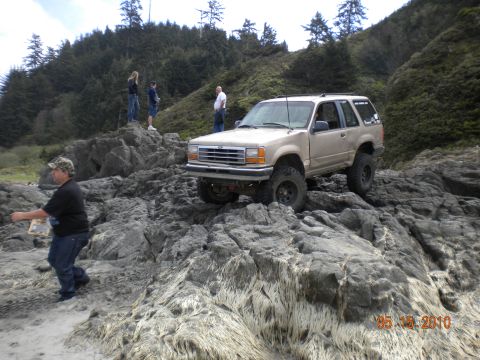 1994 Ford Explorer - A tan SUV navigates a rocky coastal landscape, with several people observing.