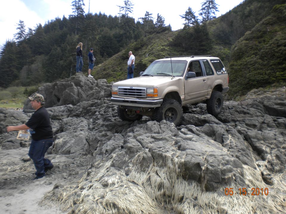 Tan two-door Ford Explorer on lifted suspension crawling over rocks with people watching