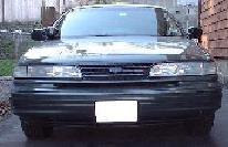 1997 Ford Crown Victoria - Low-resolution front view of a dark green or gray 1990s sedan showing the grille, headlights and hood.