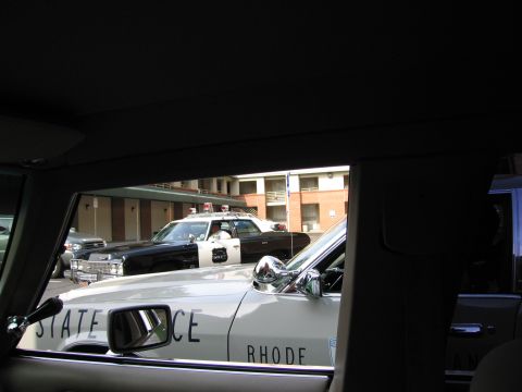 1991 Ford Crown Victoria - Two police cars are parked in front of a motel, one white and one black and white.