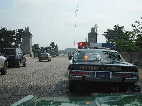 1991 Ford Crown Victoria - A police car with 'HIGHWAY PATROL' visible on the rear is seen from behind, with other vehicles on a cobblestone road.