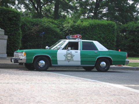 1991 Ford Crown Victoria - A vintage sheriff's patrol car, likely from the 1980s, is parked curbside with emergency lights on its roof.