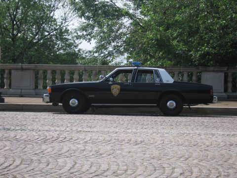 1991 Ford Crown Victoria - A black and white police car with a light bar on the roof is seen from the side.