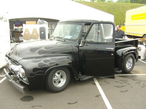 2007 Ford Mustang - A black 1950s Ford pickup truck with custom flame decals and chrome wheels is parked with its driver's door open.