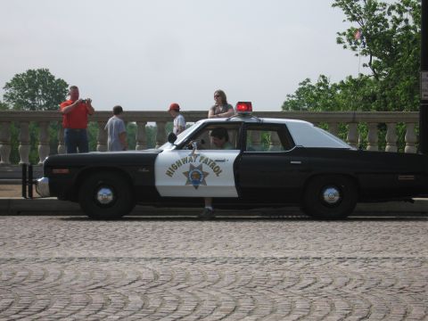 1991 Ford Crown Victoria - Side view of a vintage highway patrol car with flashing red lights on the roof.