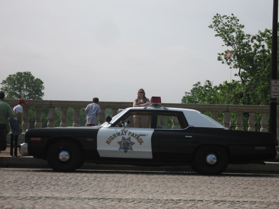 Black-and-white Highway Patrol sedan parked on a cobblestone road by a railing
