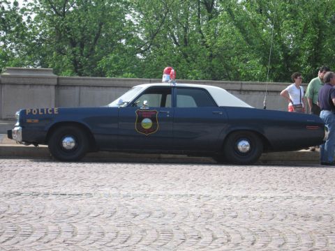 1991 Ford Crown Victoria - A dark blue police car with a white roof and a red light bar is seen from the side.