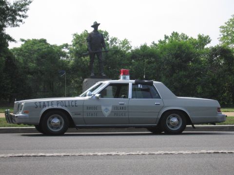 1991 Ford Crown Victoria - Side view of a Rhode Island State Police car, likely from the early 1980s, with a statue in the background.