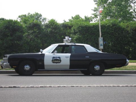 1991 Ford Crown Victoria - A two-tone police car is parked on the side of the road with trees in the background.