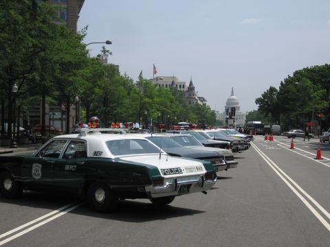 1991 Ford Crown Victoria - A line of police cars, including a green and white model with "68 PCT" on the door, are parked on a street with the Capitol building in the…