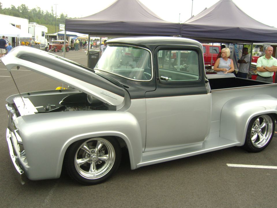 Silver and black classic pickup truck with hood open, parked at an outdoor event