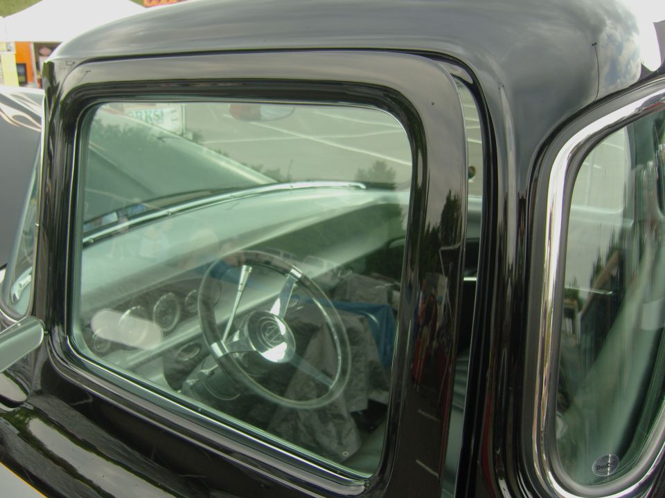 Black pickup truck interior with a chrome steering wheel and dashboard gauges visible through the driver's side window