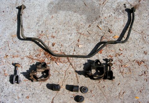 1976 Ford Ranchero - Various automotive suspension components, including a sway bar and its brackets, are displayed on a rough concrete surface.