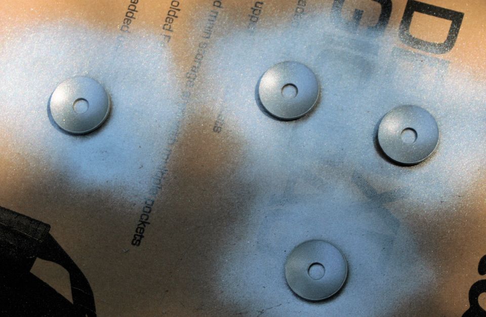 Four metal washers with center holes, being spray painted silver over a cardboard surface with text
