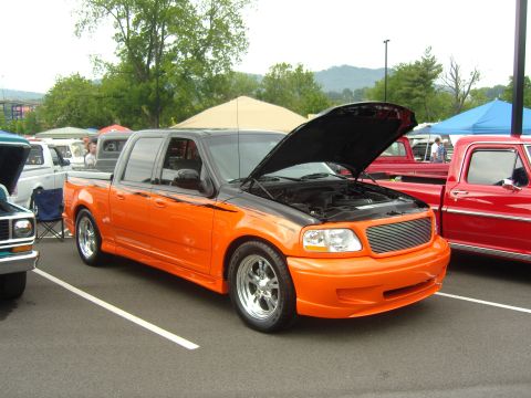 2007 Ford Mustang - Custom orange and black pickup truck with hood open at an outdoor event.