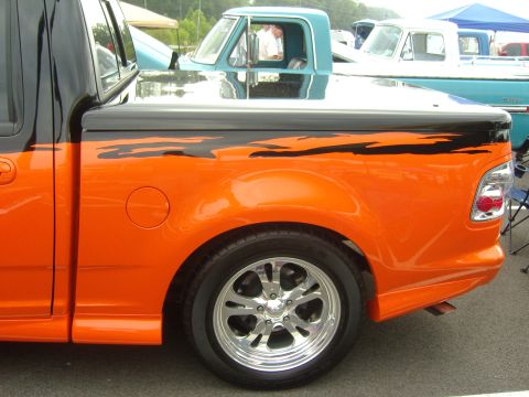 2007 Ford Mustang - An orange pickup truck with custom flame graphics is parked next to other vehicles.