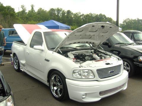 2007 Ford Mustang - A white Ford F-150 Lightning pickup truck is displayed with its hood open, parked next to another truck.