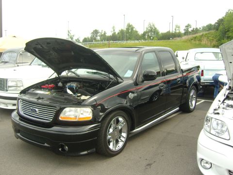 2007 Ford Mustang - A black Ford F-150 pickup truck is parked with its hood open, alongside other vehicles.