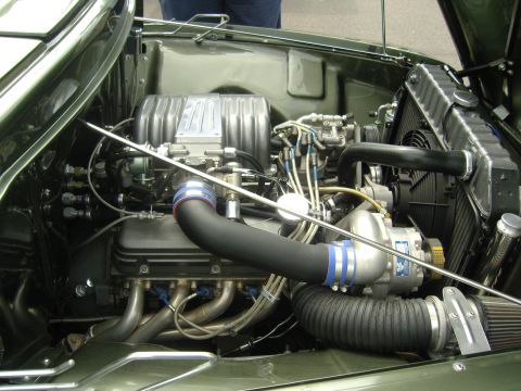 2007 Ford Mustang - The engine bay of a car shows a supercharger and custom exhaust components.