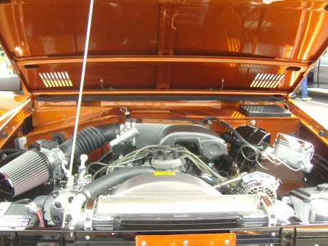 2007 Ford Mustang - The engine bay of an orange Ford Bronco, modified with chrome parts and an aftermarket air intake system.