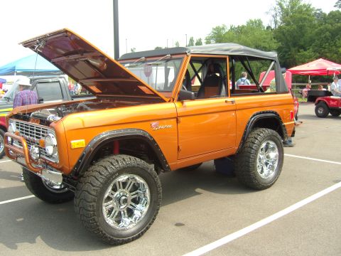 2007 Ford Mustang - This orange 1977 Ford Bronco features a lifted suspension, aftermarket chrome wheels, and its hood is propped open.