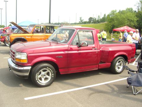 2007 Ford Mustang - Red 1990s Ford F-150 Flareside pickup parked at an outdoor car show, shown from the driver-side front three-quarter angle with a tonneau-co…
