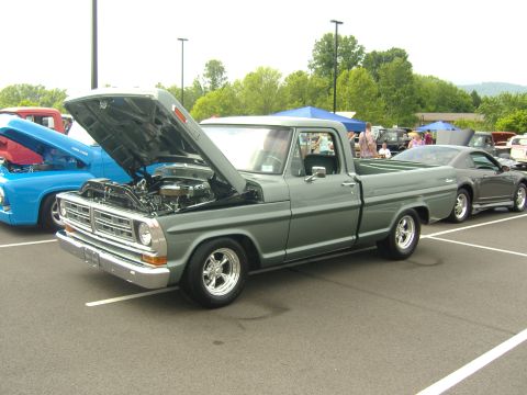 2007 Ford Mustang - Gray early-1970s Ford F-100 Ranger short-bed pickup parked at an outdoor show with the hood open, revealing a V8 with chrome valve covers a…