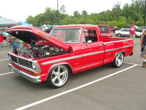 2007 Ford Mustang - Custom red pickup truck displayed at an outdoor event, hood raised to reveal engine.