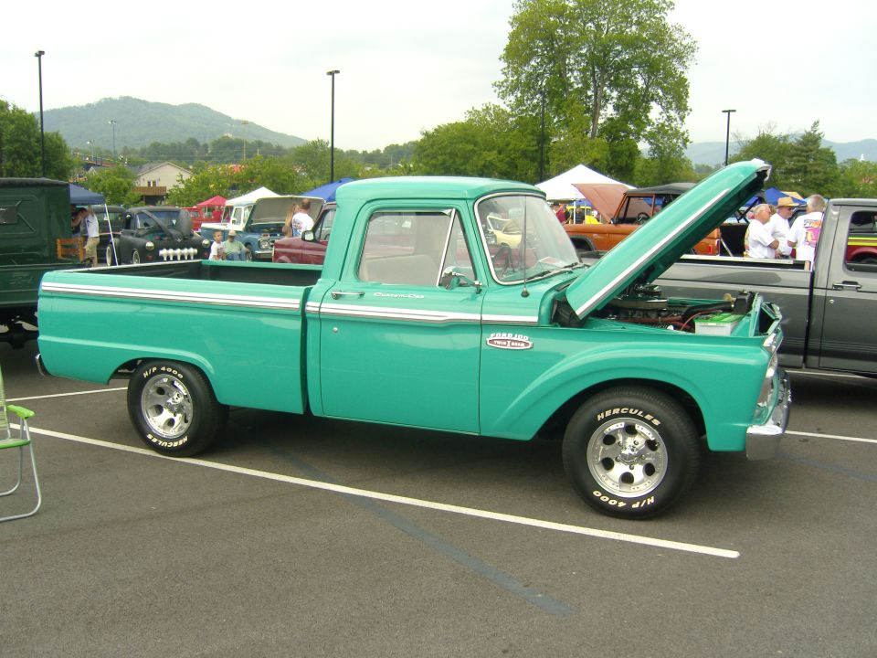 Turquoise 1956 Ford F-100 pickup truck with hood open, parked at an outdoor event