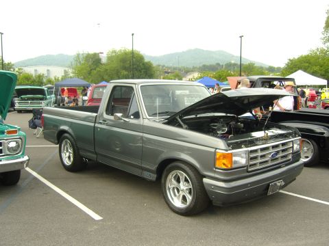 2007 Ford Mustang - A gray Ford F-150 pickup truck is displayed with its hood open at a car show, alongside other vehicles.