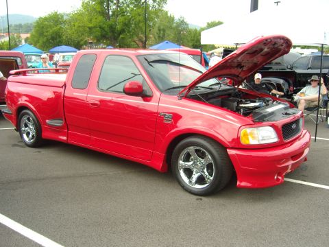2007 Ford Mustang - Red 1999 Ford F-150 Lightning pickup truck displayed with its hood open at a car show.