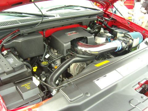 2007 Ford Mustang - The engine compartment of a red Ford truck is shown, a Triton V8 engine with a chrome intake pipe and blue air filter.