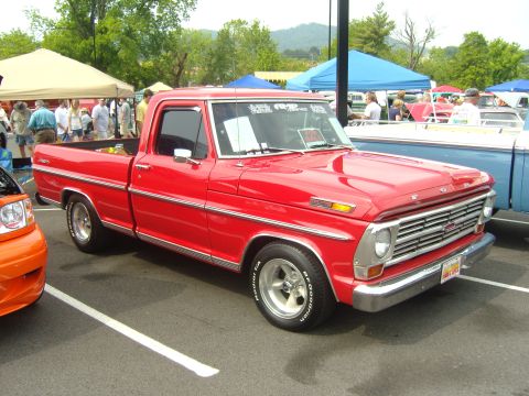 2007 Ford Mustang - A classic red pickup truck is displayed at a car show with tents and other vehicles in the background.