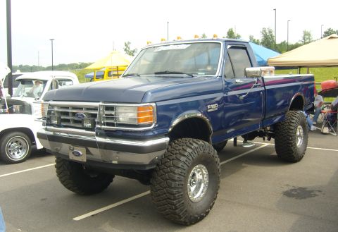 2007 Ford Mustang - Lifted blue Ford F-250 pickup truck with custom wheels and tires at an outdoor event.