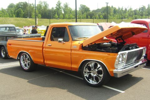 2007 Ford Mustang - Orange pickup truck with custom wheels and open hood parked at an outdoor event.