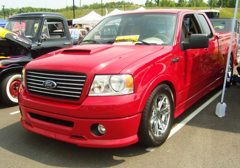 2007 Ford Mustang - Red Ford F-150 pickup truck with custom modifications is parked at an outdoor event.