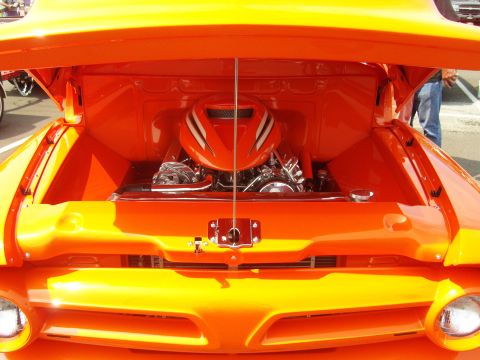2007 Ford Mustang - The engine bay of a bright orange custom truck is displayed with the hood open, revealing a polished engine and air intake.