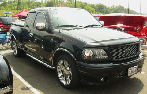 2007 Ford Mustang - A black Ford F-150 Lightning pickup truck is parked at an outdoor event, with other vehicles visible in the background.