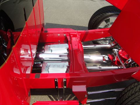 2007 Ford Mustang - Looking down under the open rear of a red hot rod or custom truck at a show, showing a red-painted frame with polished chrome Borla muffler…