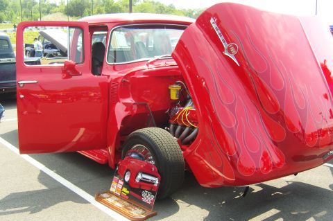 2007 Ford Mustang - A red 1956 Ford F-100 pickup truck with flame graphics on the hood and an open door and hood is displayed at a car show.