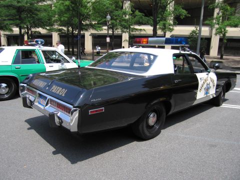 1991 Ford Crown Victoria - A vintage police car with a light bar is parked on the street next to another patrol vehicle.