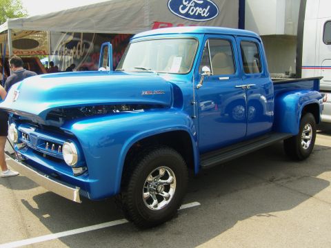 2007 Ford Mustang - A bright blue Ford F-100 pickup truck is parked under a Ford branded tent at an outdoor event.