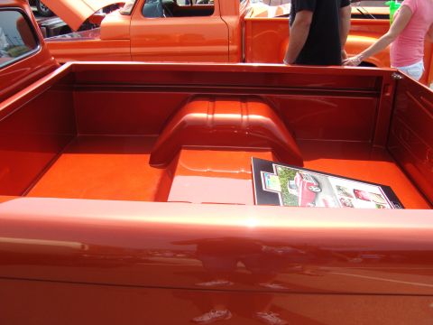 2007 Ford Mustang - The bed of a shiny orange pickup truck holds a framed display a red vehicle and other images.