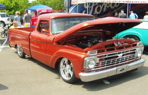 2007 Ford Mustang - A classic orange pickup truck is displayed with its hood open at an outdoor event.
