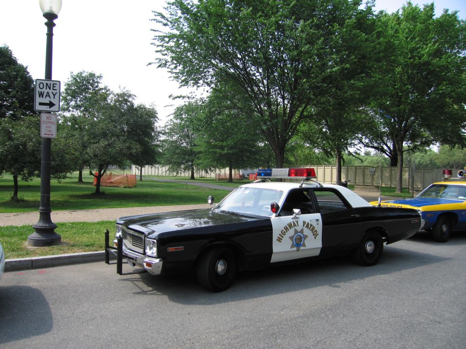 Black-and-white Dodge Highway Patrol sedan parked by a One Way sign