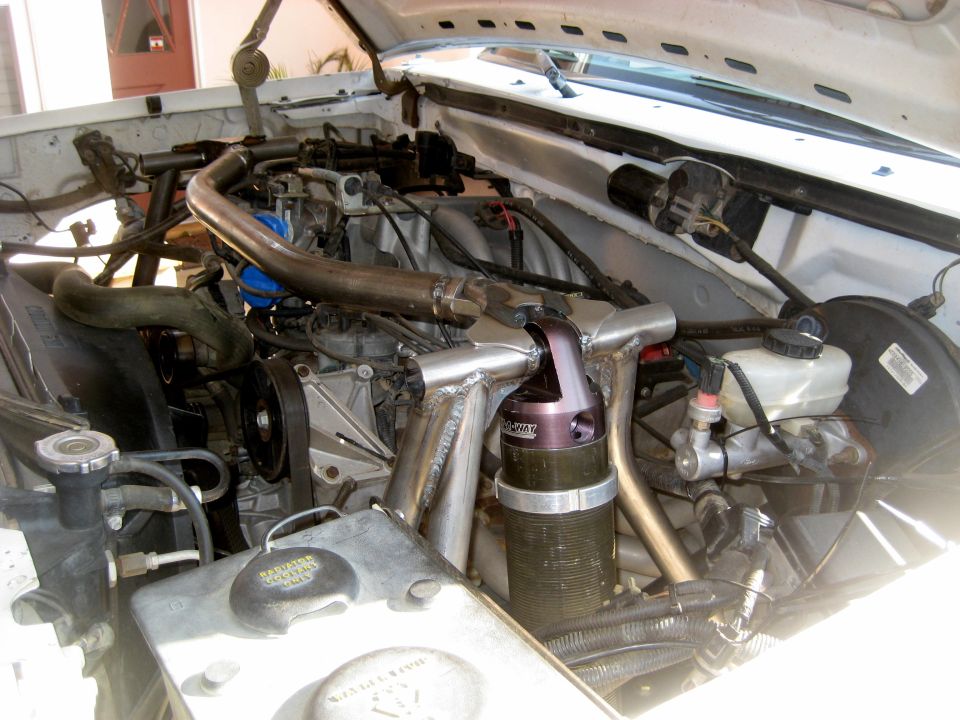 White vehicle engine bay with custom metalwork and aftermarket parts